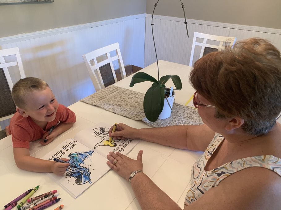 boy laughs while coloring a dinosaur with his mom